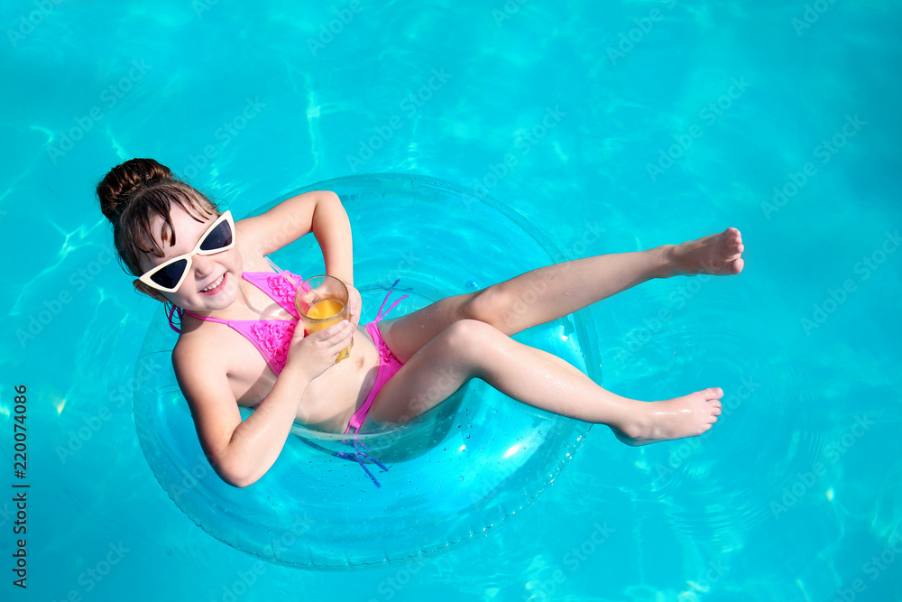 Cute girl with glass of juice swimming in pool on summer day