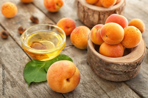 Bowl with essential oil and fresh apricots on wooden table
