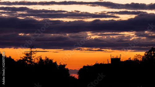 Sunset with silhouettes of trees and a building with many antennas with colorful clouds in the background