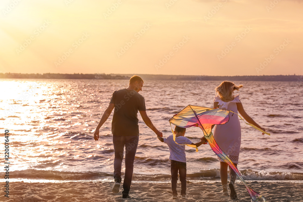Fototapeta premium Happy family flying kite near river at sunset