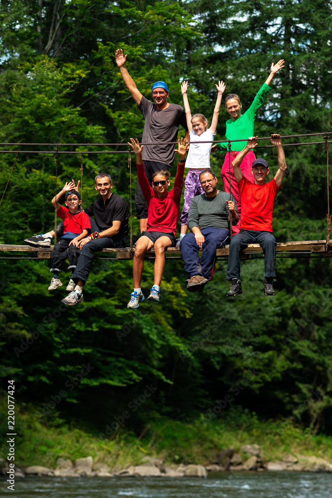 Happy travelers, friends with open arms sit on the suspension bridge