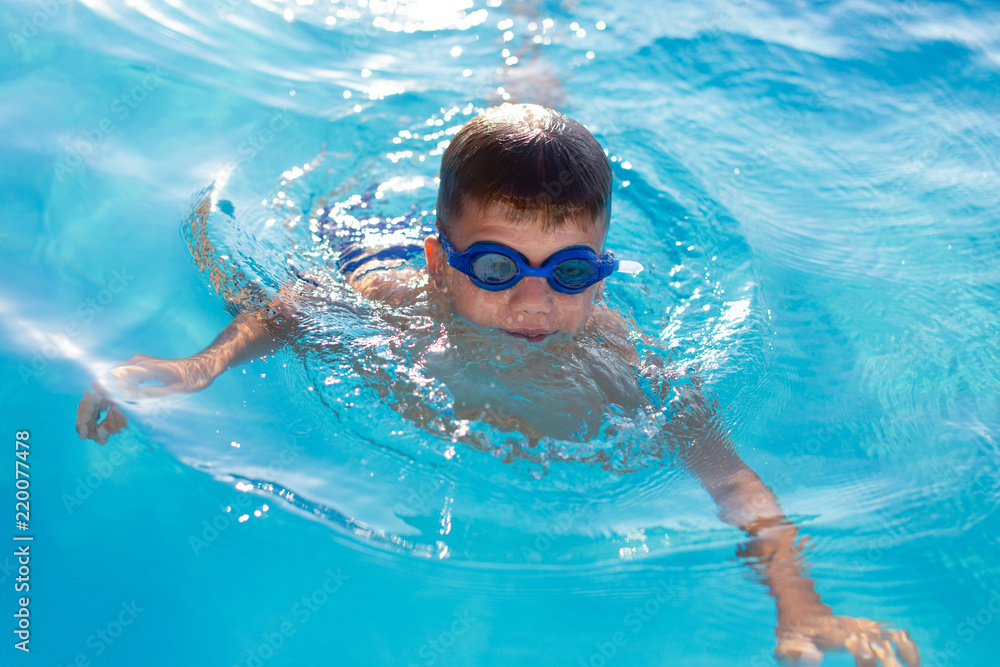 Young boy in goggles swim in swimming pool
