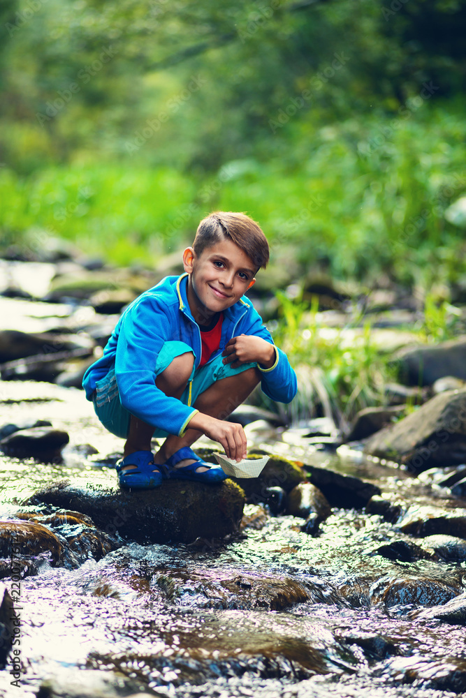 Small boy sits on the rocks next to the mountain river and smiling