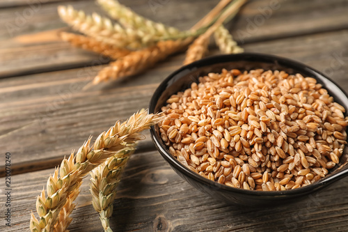 Bowl with wheat grains and spikelets on wooden table, closeup