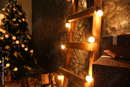 Wooden ladder with Christmas garland and gifts near dark wall indoors