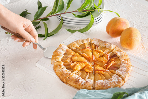 Woman taking slice of peach galette from board