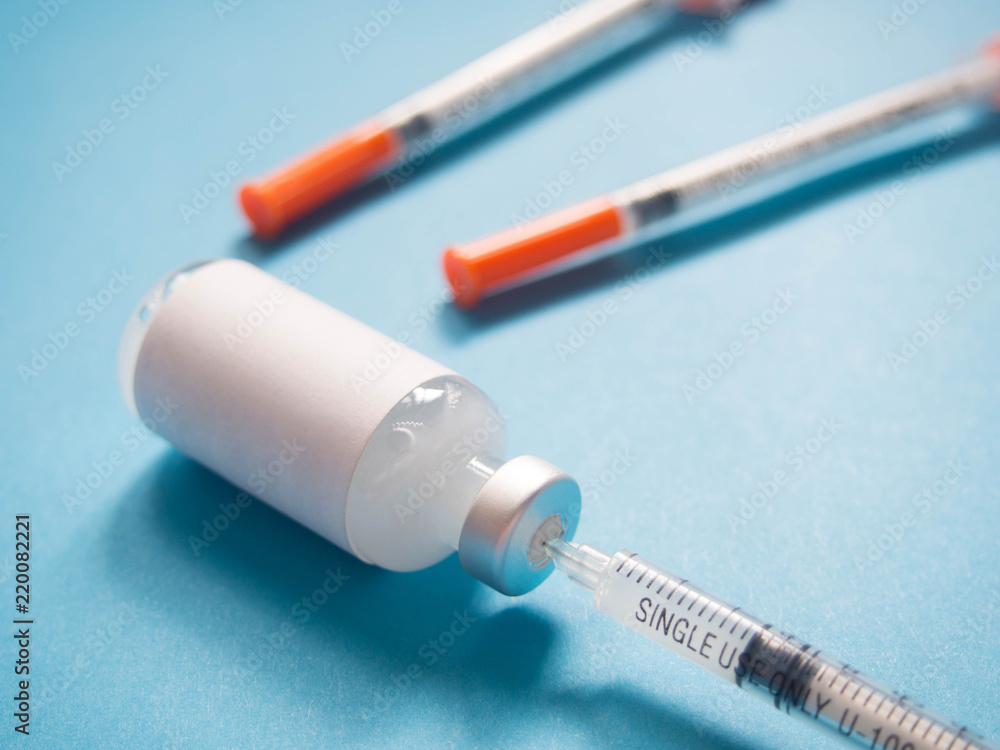 Close up of blank label medical glass vial with plastic single-use syringes on blue background. Concept of immunization, insulin hormone, vaccination, cosmetic injection and health care. Close up of blank label medical glass vial with plastic single-use syringes on blue background. Concept of immunization, insulin hormone, vaccination, cosmetic injection and health care.