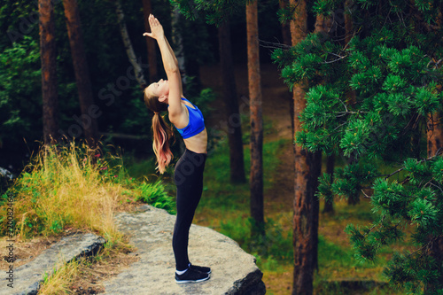 Blonde woman doing namaste, standing on a rock in the forest. Yoga nature concept.