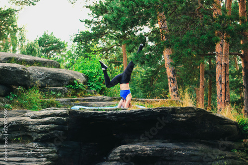Blonde woman doing headstand on a rock in the forest. Yoga nature concept.
