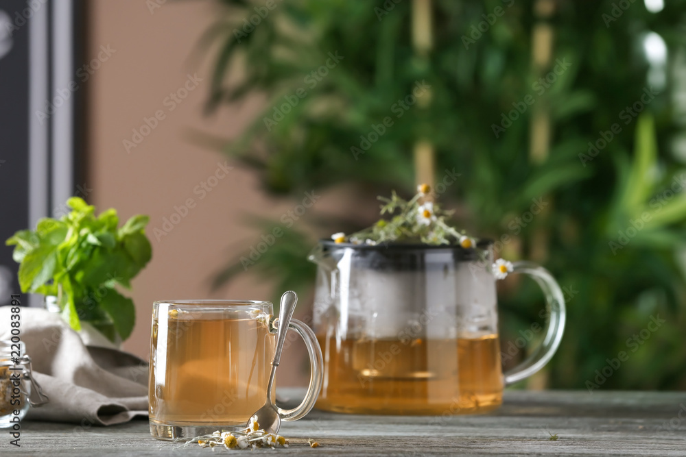 Glass cup and teapot of delicious chamomile drink on wooden table Glass cup and teapot of delicious chamomile drink on wooden table