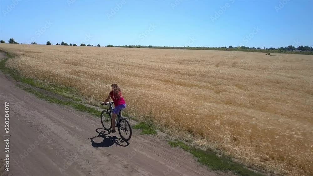 Aerial View of girl rides along the road between agricultural fields. 4K Aerial View of girl rides along the road between agricultural fields. 4K