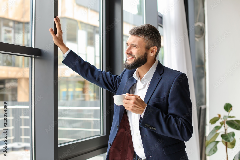 Businessman drinking coffee near window in office Businessman drinking coffee near window in office