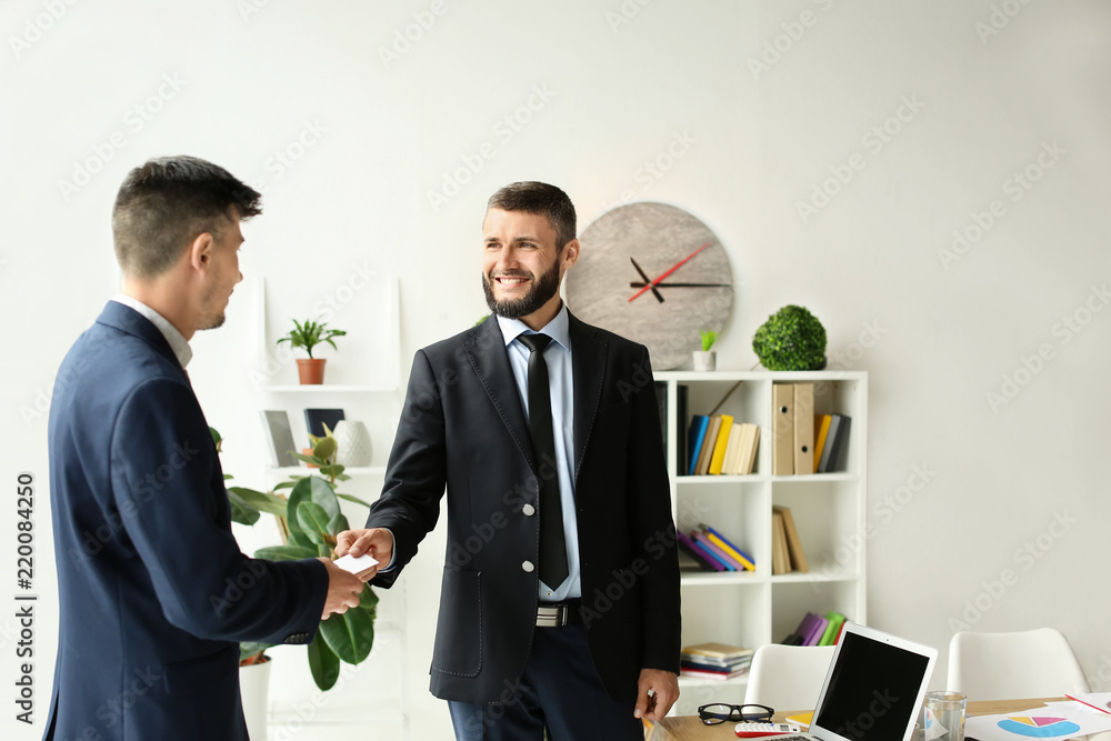 Man giving business card to colleague in office Man giving business card to colleague in office