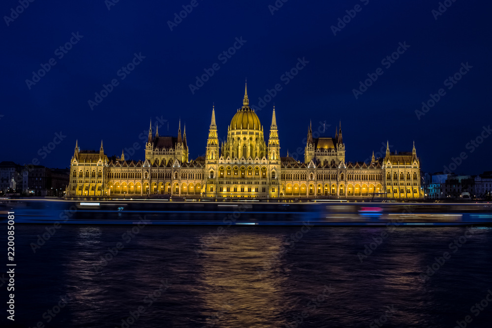 Fototapeta premium long exposure photography beautiful concept of Budapest parliament buildings architecture symmetry facade on riverfront shore with fuzzy illuminated cruise ship