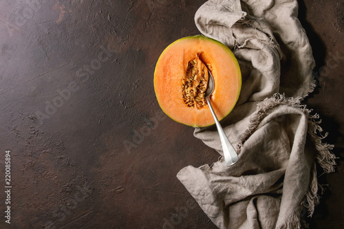 Half of ripe organic Cantaloupe melon with seeds and spoon inside on cloth textile over dark brown texture background. Flat lay, space