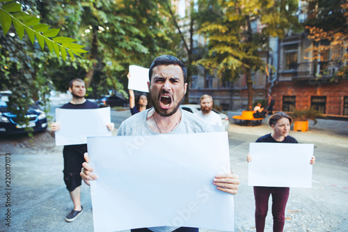 Group of protesting young people outdoors. The protest, people, demonstration, democracy, fight, rights, protesting concept. The caucasian men and womem holding empty posters or banners with copy photo