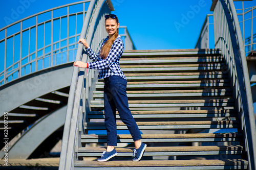 Young stylish girl stands on street stairs in sunny day. Street style