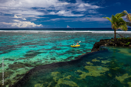 Female and little boy paddling canoe on a lagoon with coral reef.