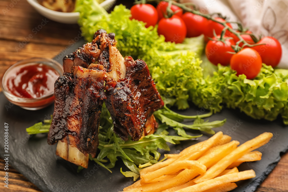 Delicious grilled ribs with vegetables, french fries and sauce on slate plate