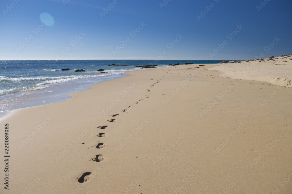 Footprints on the sand near the sea with rocks in the beach