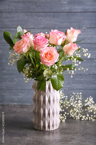 Vase with beautiful roses on grey table