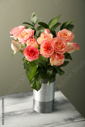 Vase with beautiful roses on wooden table against grey background © Pixel-Shot