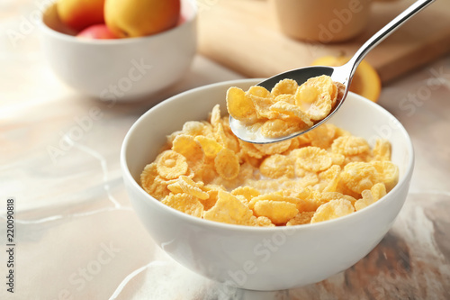 Photo Eating of healthy cornflakes with milk from bowl on table, closeup