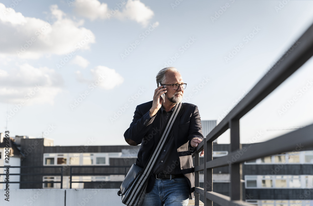 Mature man standing on rooftop, leaning on railing, using smartphone Mature man standing on rooftop, leaning on railing, using smartphone