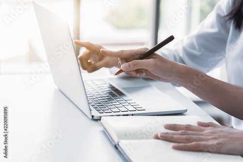 Close up of two businesswoman using laptop and writing on notebook in the morning. Business and financial concept. People and lifestyles concept. Office and workplace theme.