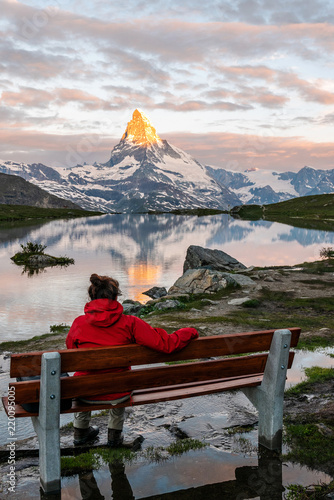Morning shot of the golden Matterhorn (Monte Cervino, Mont Cervin) pyramid and  blue Stellisee lake. Female tourist enjoying view of early morning Matterhorn mountain is Valais Alps, Switzerland.