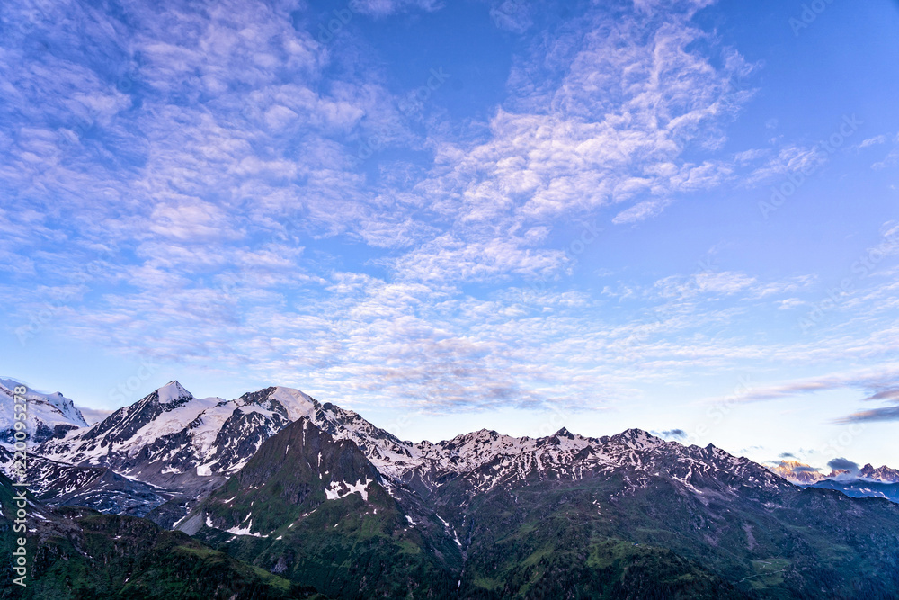 Scenic view of beautiful landscape in Swiss Alps. Fresh green meadows and snow-capped mountain tops in the background in springtime, Switzerland.