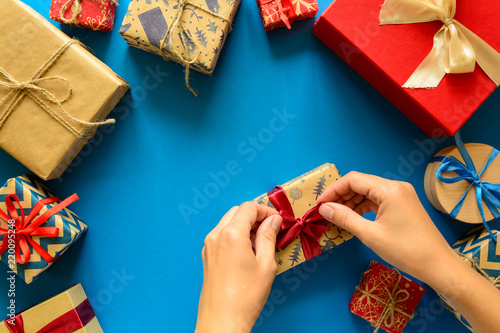 Woman's hands decorate present box on paper background. New Year, holidays and celebration decorations concept. Copy space. Flat lay