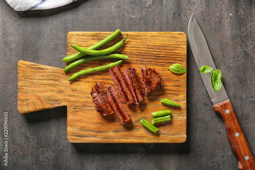 Cut grilled steak with green beans on wooden board