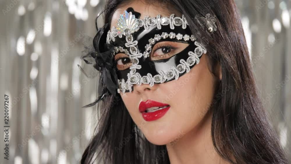 Sexy woman wearing masquerade mask flirting at party over silver glitter background, slow motion. Sexy woman wearing masquerade mask flirting at party over silver glitter background, slow motion.