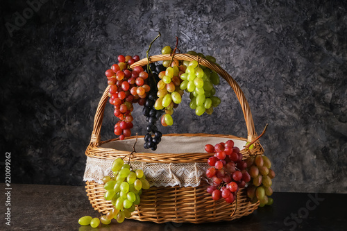 Wicker basket with fresh ripe grapes on dark grey background