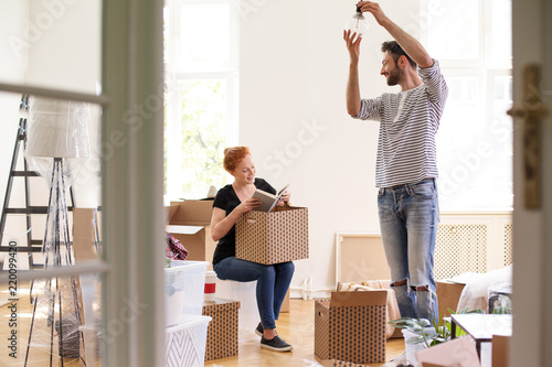 Man hanging lamp while smiling woman unpacking stuff from boxes photo