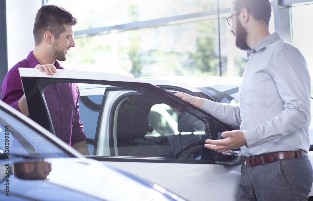New buyer getting into a car in a showroom. Car dealer standing next to a car New buyer getting into a car in a showroom. Car dealer standing next to a car