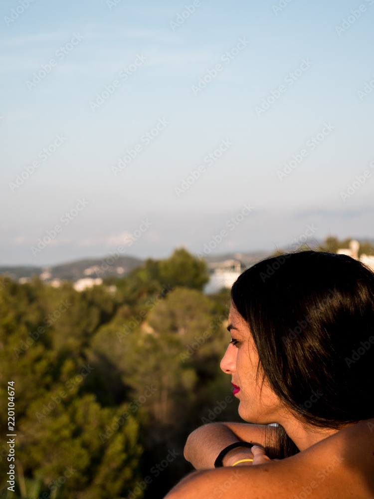 Beautiful young woman in profile looking from a balcony at the horizon with lots of vegetation around her Beautiful young woman in profile looking from a balcony at the horizon with lots of vegetation around her