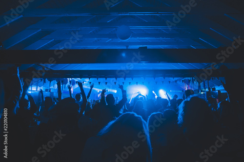 Crowd of audience with hands raised at a music festival. Lights streaming down from above the stage