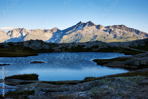 Blick auf Bergkette mit Mittaghorn, felsiger Vordergrund mit Bergsee im schattigen Abendlicht, blauer Himmel photo