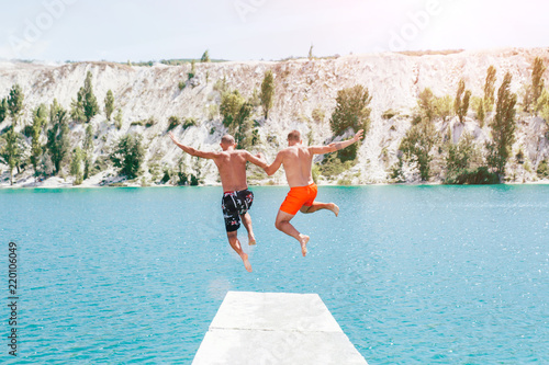 Gay men couple jumping in blue lake.