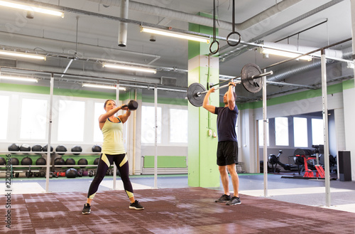 sport, fitness, weightlifting, lifestyle and people concept - man and woman with kettlebell and barbell exercising in gym