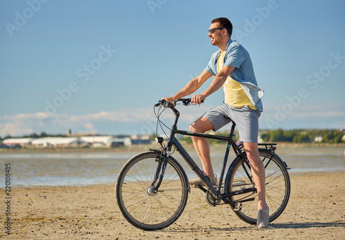 people, leisure and lifestyle concept - happy young man riding bicycle along summer beach