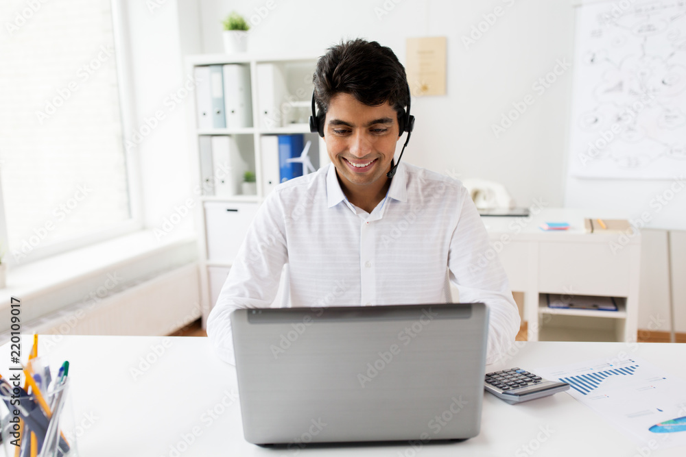 communication, business, people and technology concept - businessman or helpline operator with headset and laptop computer typing at office communication, business, people and technology concept - businessman or helpline operator with headset and laptop computer typing at office