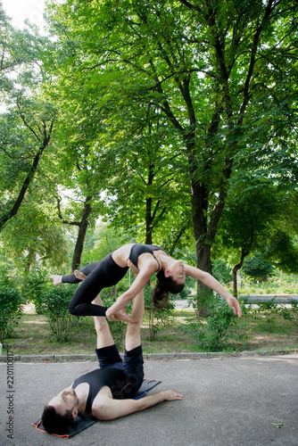 Young athletic couple practicing acroyoga in park urban style.Balancing in pair. Fit active pair yoga time.Sporty handsome man supporting slim beautiful brunette woman.Training time.Asana 