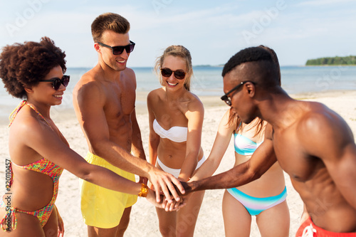 friendship, summer holidays and people concept - group of happy friends stacking hands together on beach