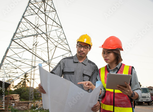 Engineers are consulting at the construction site,Asian women engineer pointing at the blue print with engneer man,Asian engineers are consulting with high voltage pole background photo