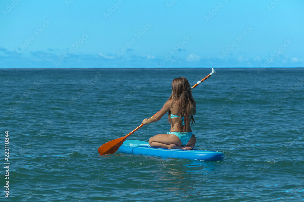Young beautiful woman in a bikini on a SUP board in the sea