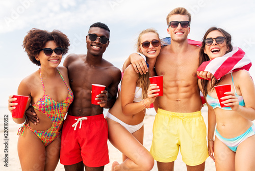 summer, holidays and people concept - group of happy friends with flag and non alcoholic drinks celebrating american independence day and party on beach