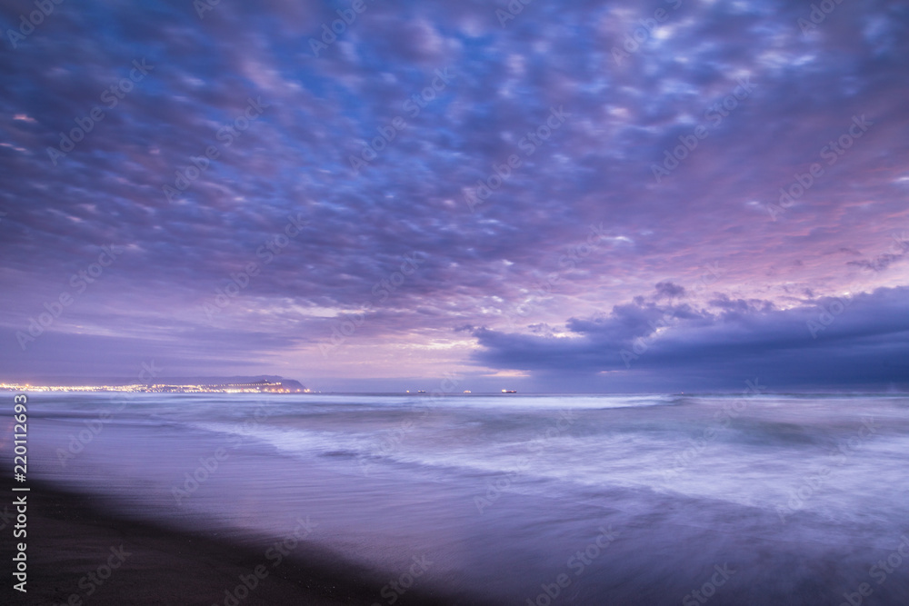 Las Machas Beach. Clouds with the last sunrays impacting over it creating an amazing palette on an infinite horizon, enjoying twilight lights over a colorful sky at Arica, Chile
